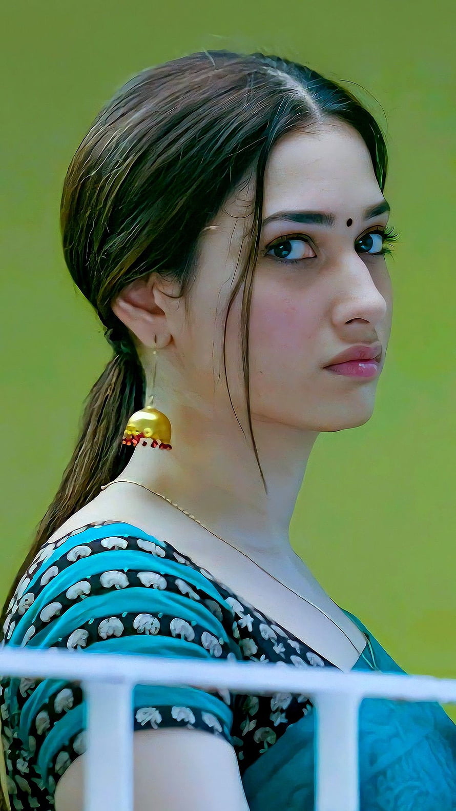 Disha Patani in a blue and black printed saree with traditional gold jhumka earrings and a bindi, looking over her shoulder against a green background HD phone wallpaper