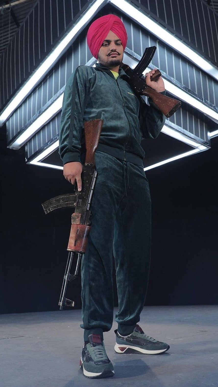 Sidhu Moose Wala in Green Tracksuit and Pink Turban Holding Rifles on Stage HD phone wallpaper