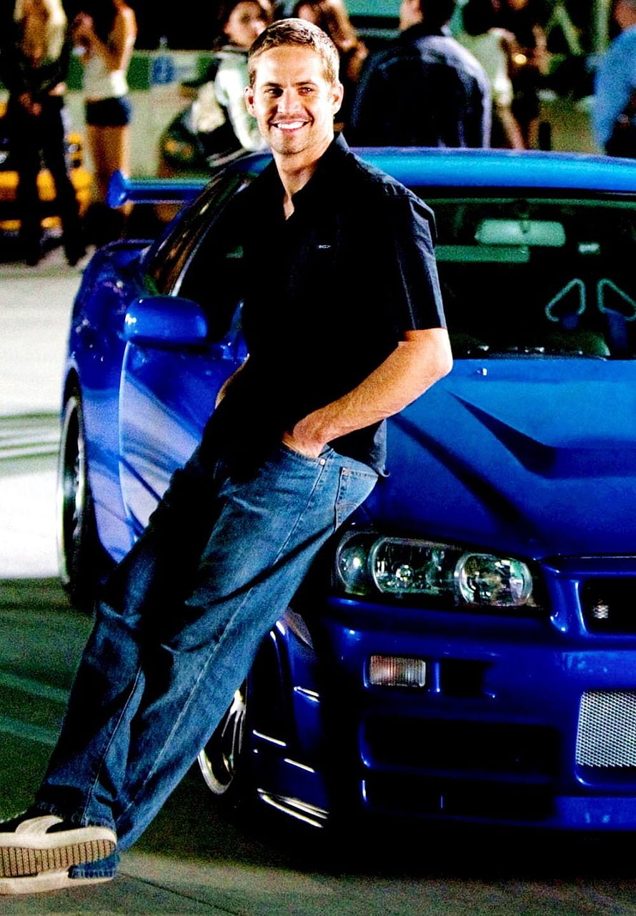 Paul Walker leaning against a blue Nissan Skyline GT-R R34 in a casual pose HD phone wallpaper