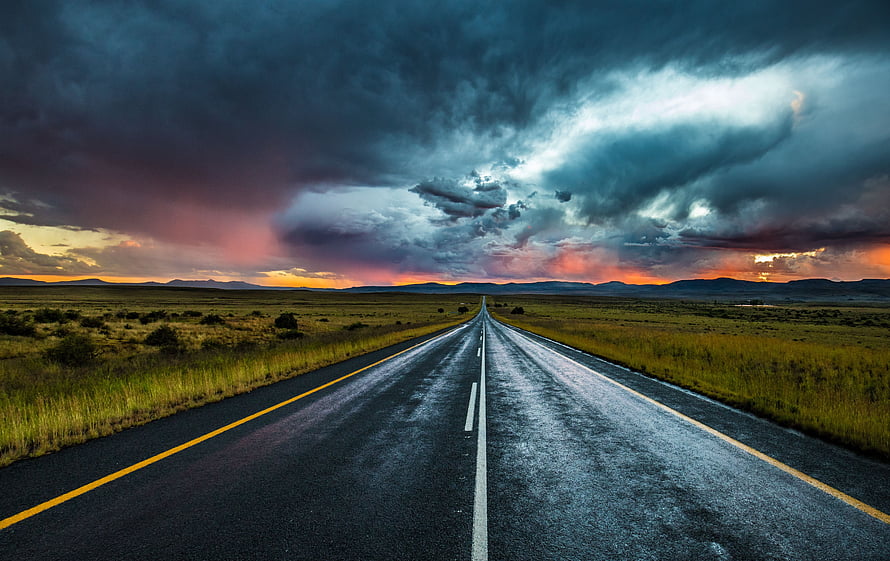 Dramatic Storm Clouds Over a Long Straight Highway at Sunset HD wallpaper