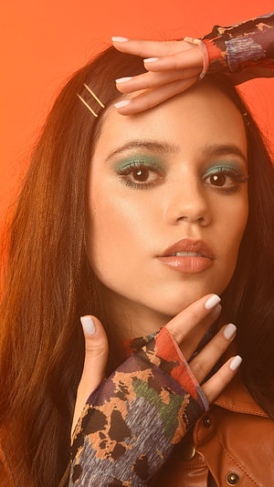 Portrait of a woman with teal eyeshadow and patterned sleeves posing against an orange background, Jenna Ortega, model, actress HD phone wallpaper