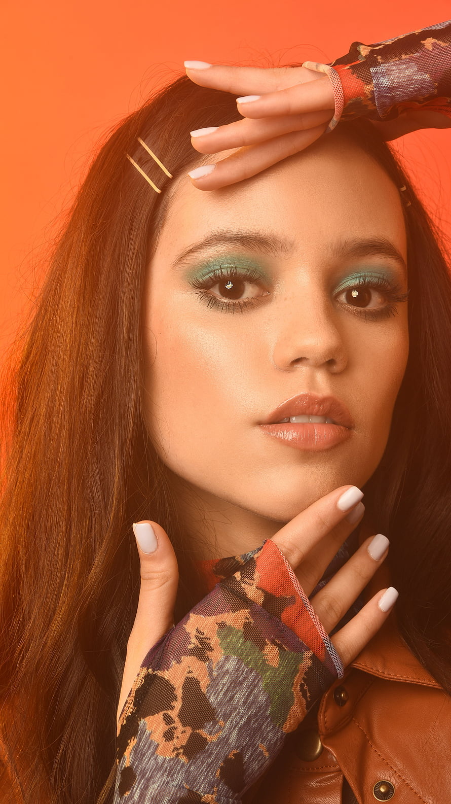 Portrait of a woman with teal eyeshadow and patterned sleeves posing against an orange background, Jenna Ortega, model, actress HD phone wallpaper