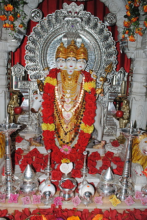 Three-headed Hindu deity statue adorned with red roses and gold jewelry in a temple shrine HD phone wallpaper