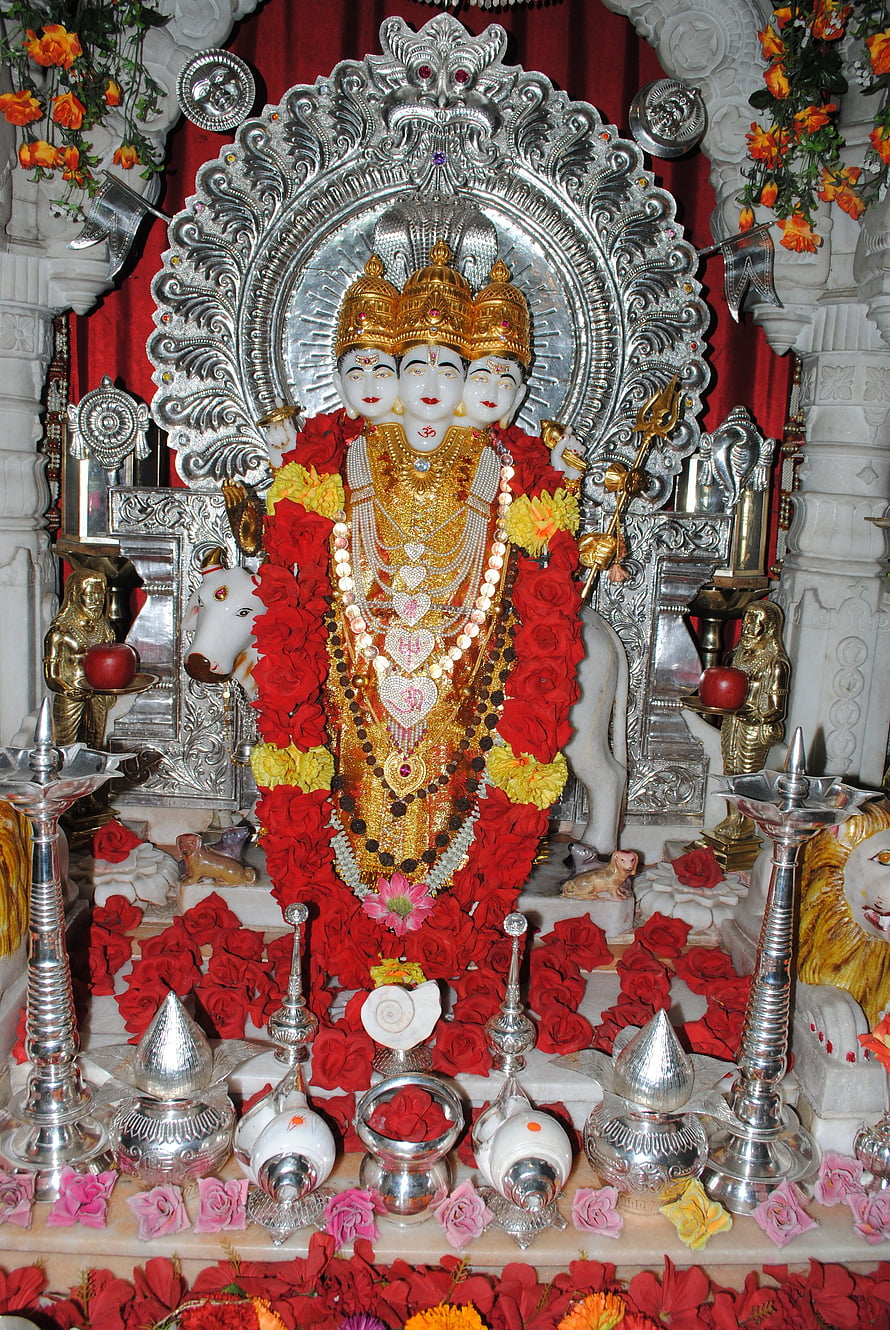 Three-headed Hindu deity statue adorned with red roses and gold jewelry in a temple shrine HD phone wallpaper