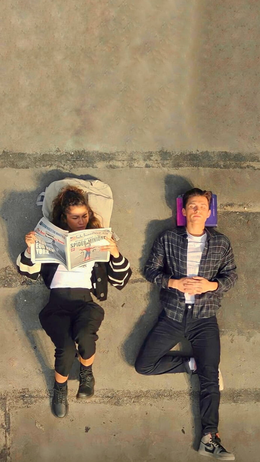 Tom Holland and Zendaya relaxing on concrete with newspaper and books HD phone wallpaper