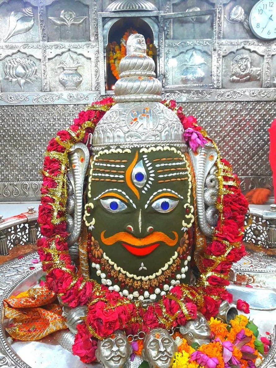 Sacred Shiva Lingam adorned with vibrant red flower garlands and intricate silver decorations in a temple setting HD phone wallpaper