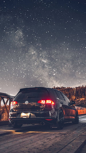 Black Volkswagen Golf GTI parked on a wooden bridge under a starry night sky HD phone wallpaper