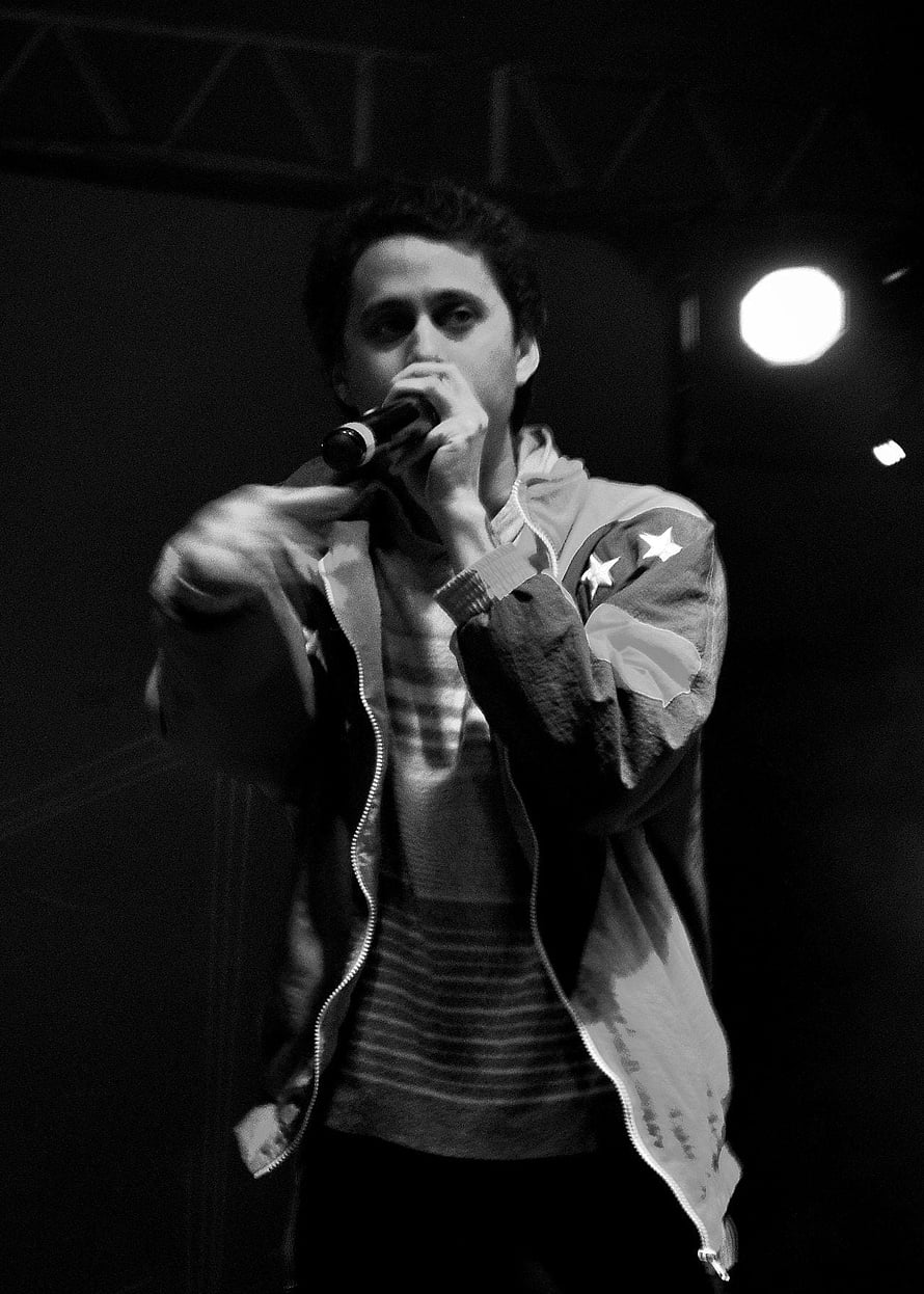 Canserbero performing live on stage in black and white with microphone and star jacket HD phone wallpaper