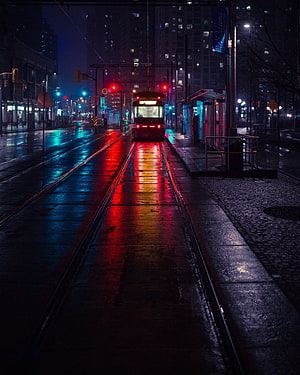 Neon-lit tram tracks on a wet city street at night with vibrant red and blue reflections HD phone wallpaper
