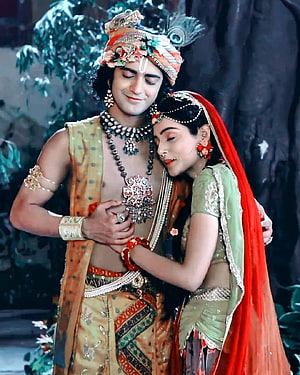 Radha and Krishna embracing in traditional attire with peacock feather crown and floral jewelry HD phone wallpaper