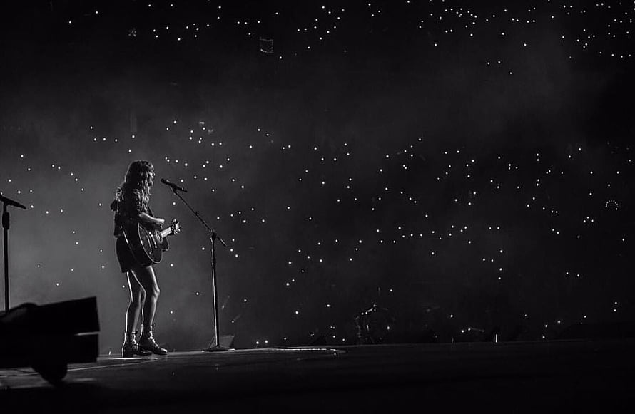 Taylor Swift performing solo with acoustic guitar on a dark concert stage under starry lights HD wallpaper