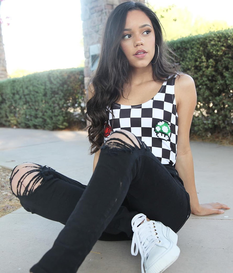 Jenna Ortega in a checkered tank top and distressed black jeans sitting outdoors HD phone wallpaper