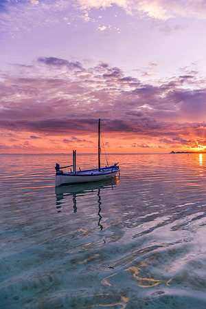 Serene Sailboat Anchored in Turquoise Waters Under a Vibrant Purple and Orange Sunset Sky HD phone wallpaper