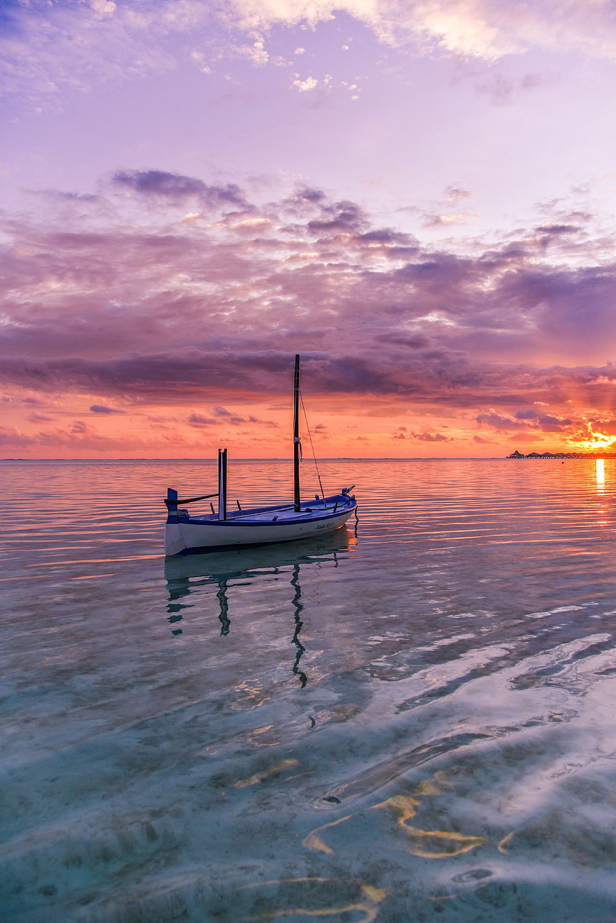 Serene Sailboat Anchored in Turquoise Waters Under a Vibrant Purple and Orange Sunset Sky HD phone wallpaper