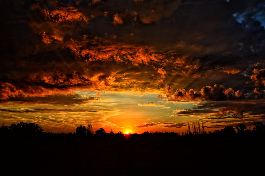 Dramatic Orange Sunset Sky with Dark Clouds Over Silhouetted Horizon HD wallpaper