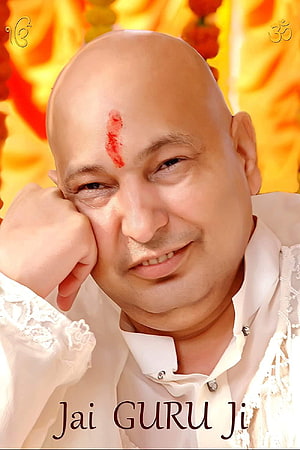 Portrait of a bald spiritual guru with a red tilak on his forehead, wearing white traditional attire against a yellow floral background HD phone wallpaper
