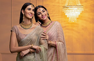 Two women in elegant sarees wearing traditional Indian gold jewelry and maang tikka HD wallpaper
