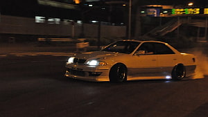 White Nissan Skyline R34 drifting on city street at night with smoke HD wallpaper