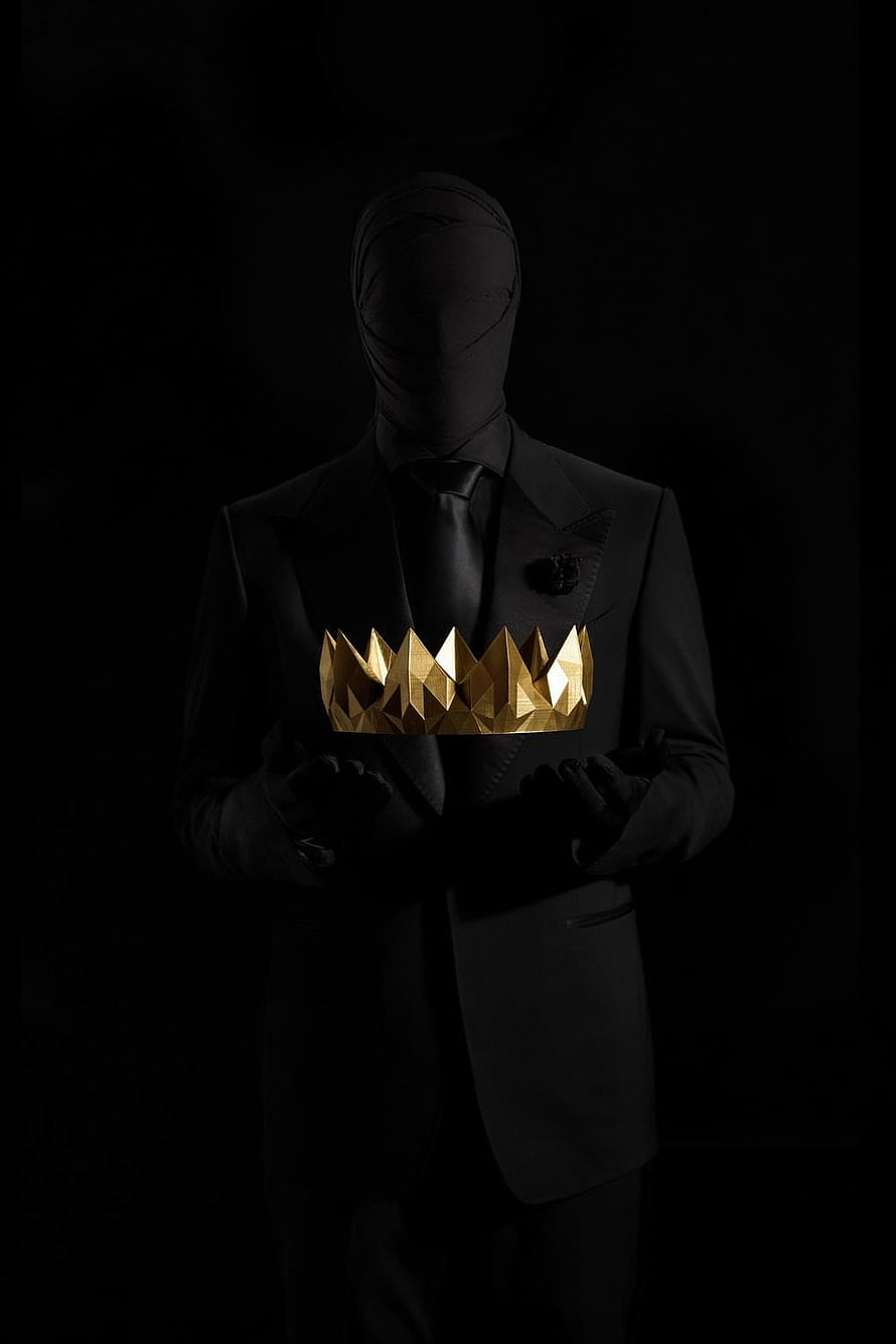 Faceless figure in a black suit holding a faceted gold crown against a dark background HD phone wallpaper
