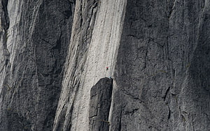 Solo Rock Climber Ascending a Massive Granite Cliff Face in a Dramatic Natural Landscape HD wallpaper