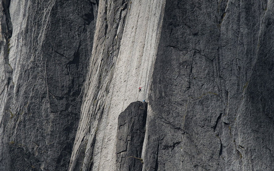 Solo Rock Climber Ascending a Massive Granite Cliff Face in a Dramatic Natural Landscape HD wallpaper