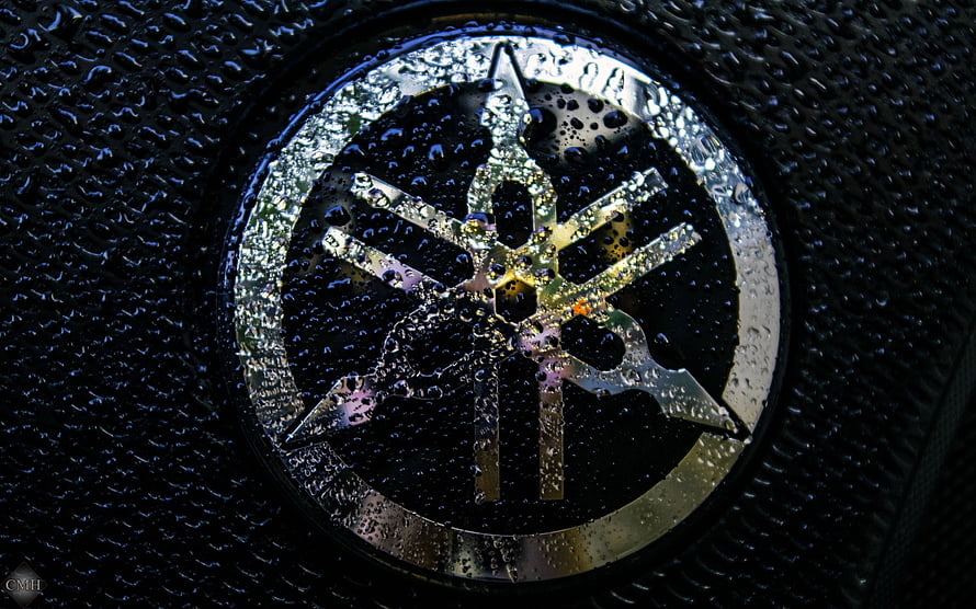 Yamaha Tuning Fork Emblem Close-Up with Water Droplets on Dark Surface HD wallpaper