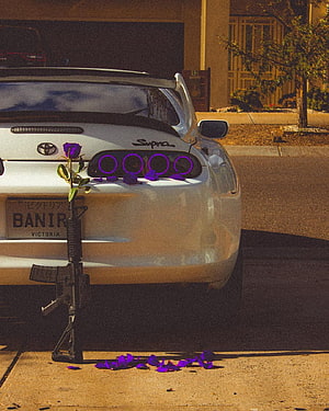 White Toyota Supra with purple rose and rifle leaning against bumper HD phone wallpaper