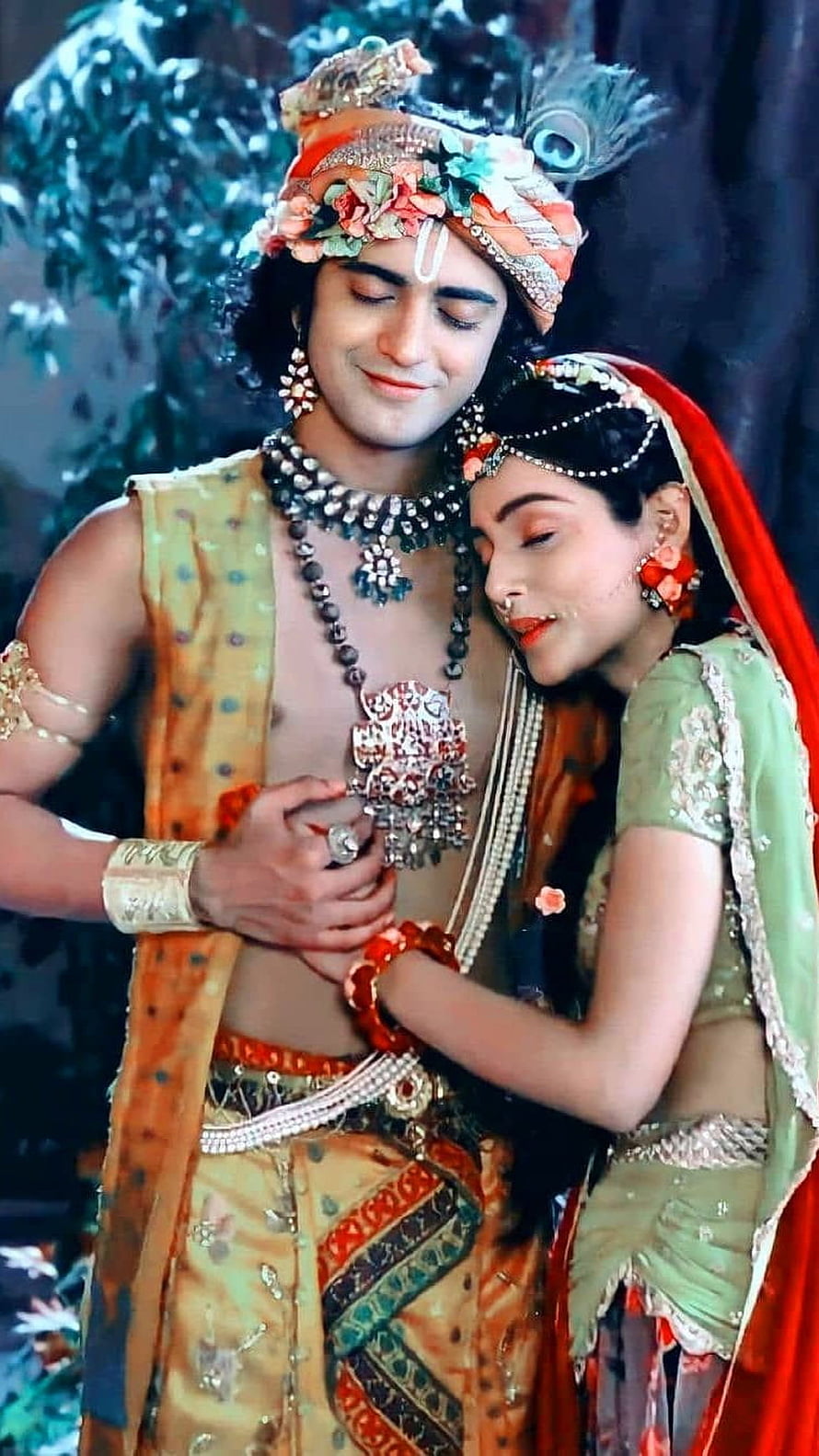 Radha and Krishna embracing in traditional attire with peacock feather crown and jewelry HD phone wallpaper