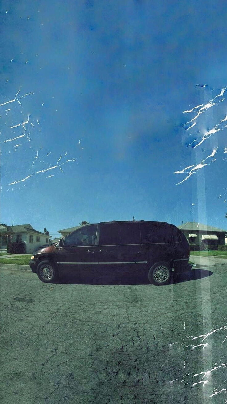 Black minivan parked on cracked asphalt under a clear blue sky in a suburban neighborhood HD phone wallpaper
