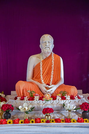 White Statue of Buddhist Monk in Orange Robes with Flower Offerings HD phone wallpaper