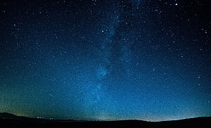 Milky Way Galaxy Arching Over a Dark Horizon Under a Deep Blue Starry Night Sky HD wallpaper