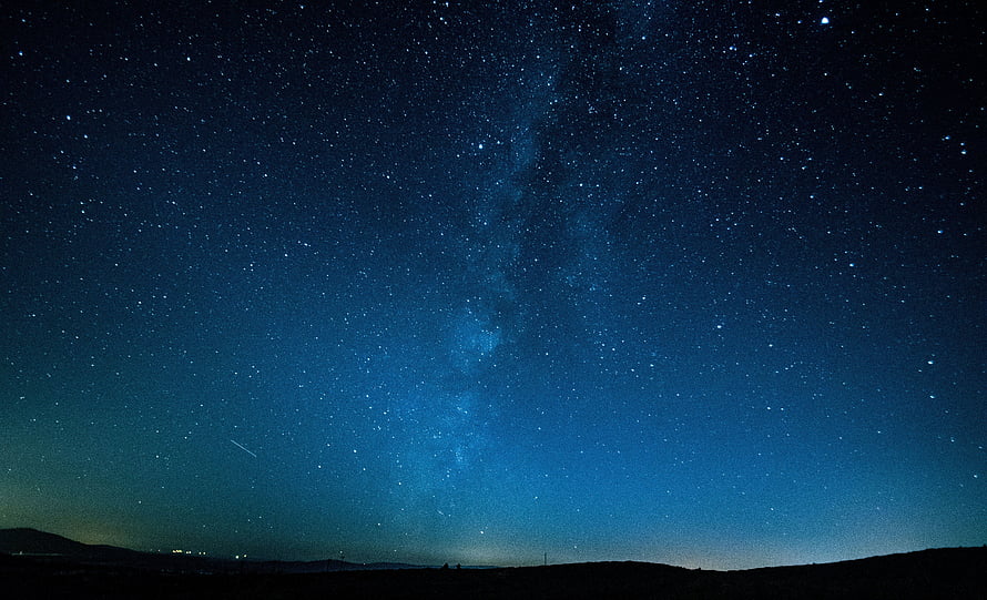 Milky Way Galaxy Arching Over a Dark Horizon Under a Deep Blue Starry Night Sky HD wallpaper