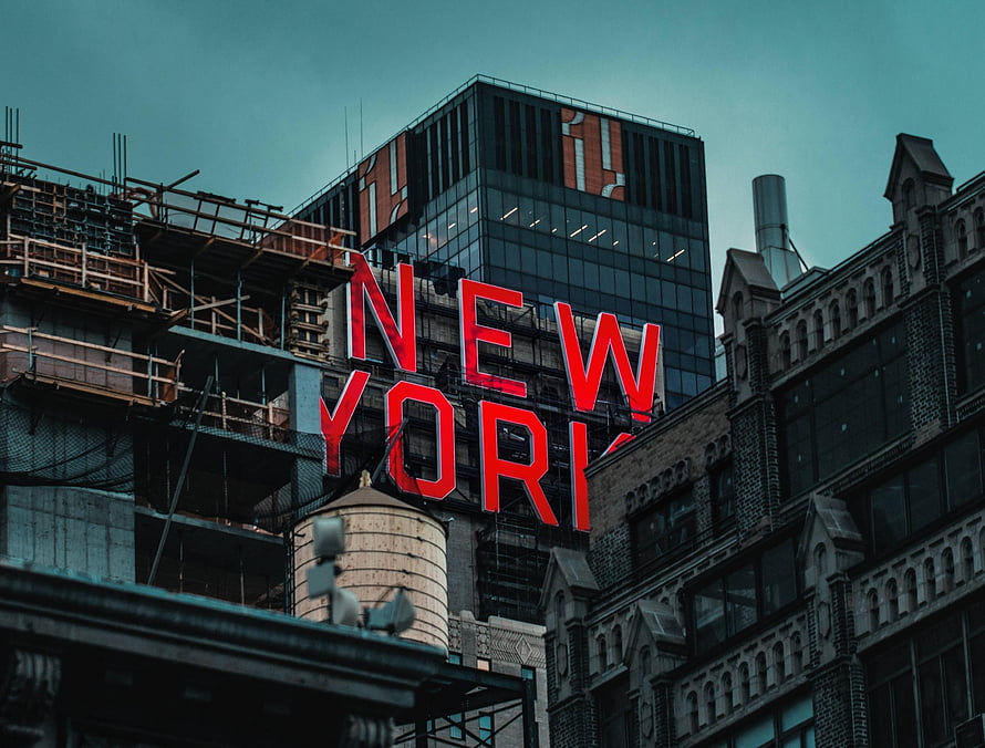New York City skyline featuring the iconic red neon sign against a backdrop of historic brick architecture and modern glass towers HD wallpaper