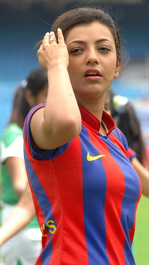 Kajal Agarwal in a red and blue striped sports jersey at a stadium event HD phone wallpaper
