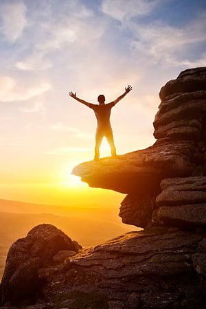 Silhouette of a man standing on a rocky cliff edge with arms raised against a golden sunset sky, Happy Man, Happy Alone HD phone wallpaper