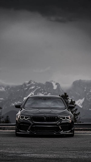 Black BMW M5 Front View on Mountain Road with Snowy Peaks and Dark Stormy Sky HD phone wallpaper