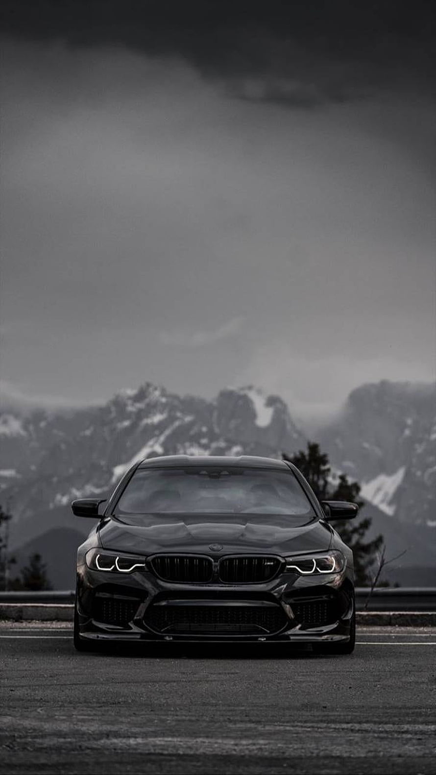 Black BMW M5 Front View on Mountain Road with Snowy Peaks and Dark Stormy Sky HD phone wallpaper