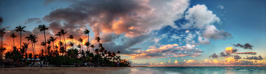 Panoramic tropical beach sunset with palm trees silhouetted against dramatic orange and blue clouds HD wallpaper