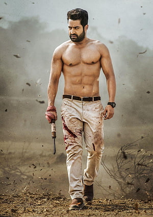 Jr. NTR shirtless action still with blood-stained trousers and knife in dusty battlefield HD phone wallpaper