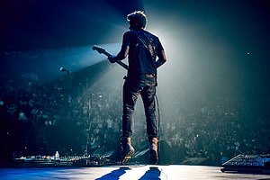 John Mayer performing live on stage with electric guitar under dramatic blue concert lighting HD wallpaper