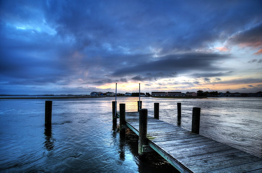 Moody Twilight Pier Over Calm Water With Distant Shoreline and Dramatic Clouds HD wallpaper