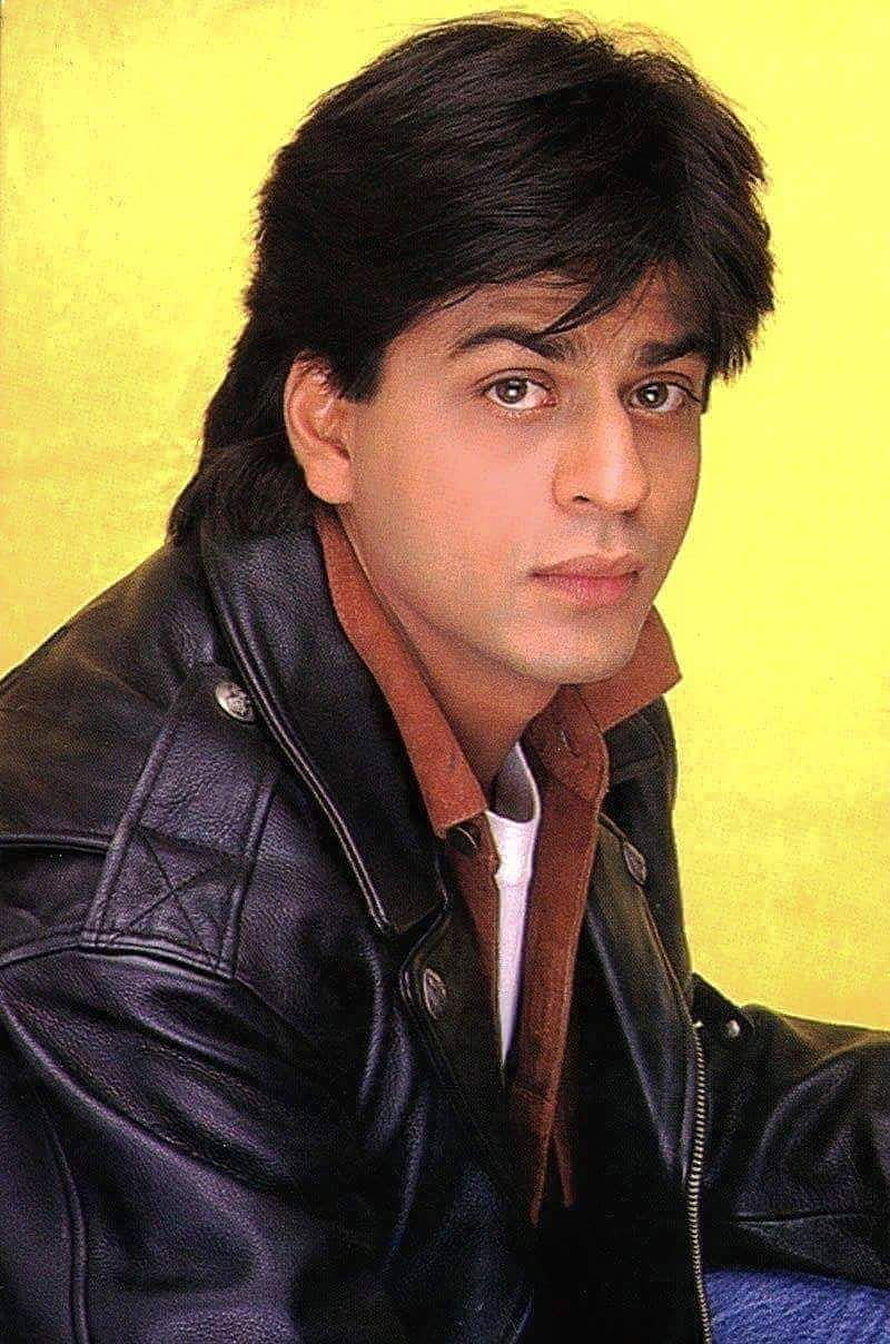 Shah Rukh Khan in a black leather jacket and brown shirt against a yellow background HD phone wallpaper