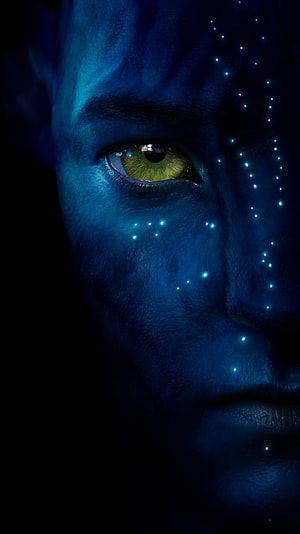 Close-up of a blue-skinned Na'vi face with glowing bioluminescent dots and a striking green eye from the Avatar film HD phone wallpaper