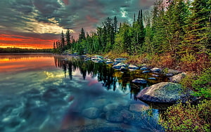 Dramatic Sunset Over a Calm Forest Lake with Rocky Shoreline and Pine Trees HD wallpaper