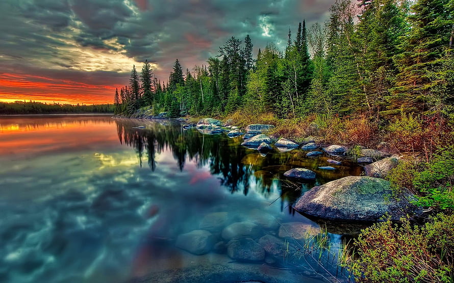 Dramatic Sunset Over a Calm Forest Lake with Rocky Shoreline and Pine Trees HD wallpaper
