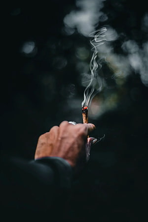 Hand Holding Lit Cigarette With Rising Smoke Against Dark Blurred Background HD phone wallpaper
