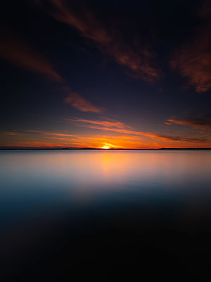 Serene Sunset Over Calm Water With Vibrant Orange And Purple Sky Reflections HD phone wallpaper