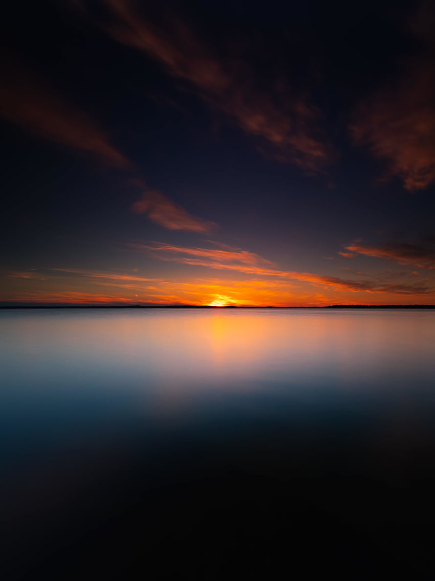 Serene Sunset Over Calm Water With Vibrant Orange And Purple Sky Reflections HD phone wallpaper