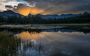Golden Sunset Rays Over Mountain Range Reflected in Calm Lake with Pine Forest HD wallpaper