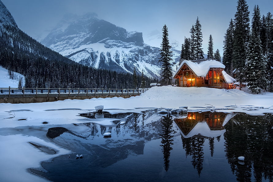 Snow-Covered Mountain Lodge with Warm Lights Reflected in a Frozen Lake at Dusk HD wallpaper